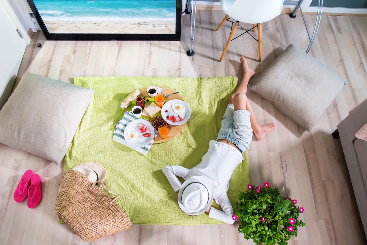 woman "vacations" at home lying on blanket with food and beach on tv 339963805