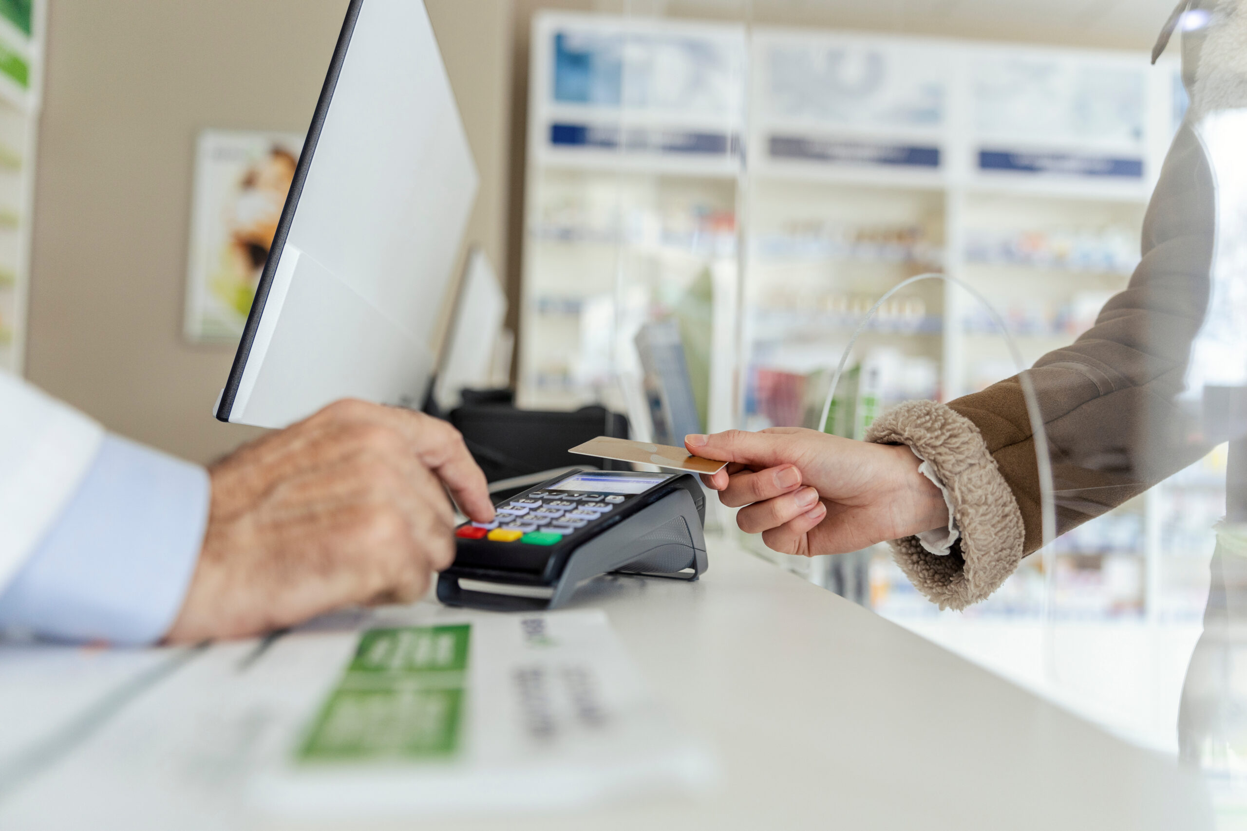 Payment of drug bills. A close-up of the payment terminal at the counter and sweeping the card for the purchase of medicines in the pharmacy. Female and male hands in focus Payment of drug bills. A close-up of the payment terminal at the counter and sweeping the card for the purchase of medicines in the pharmacy. Female and male hands in focus.